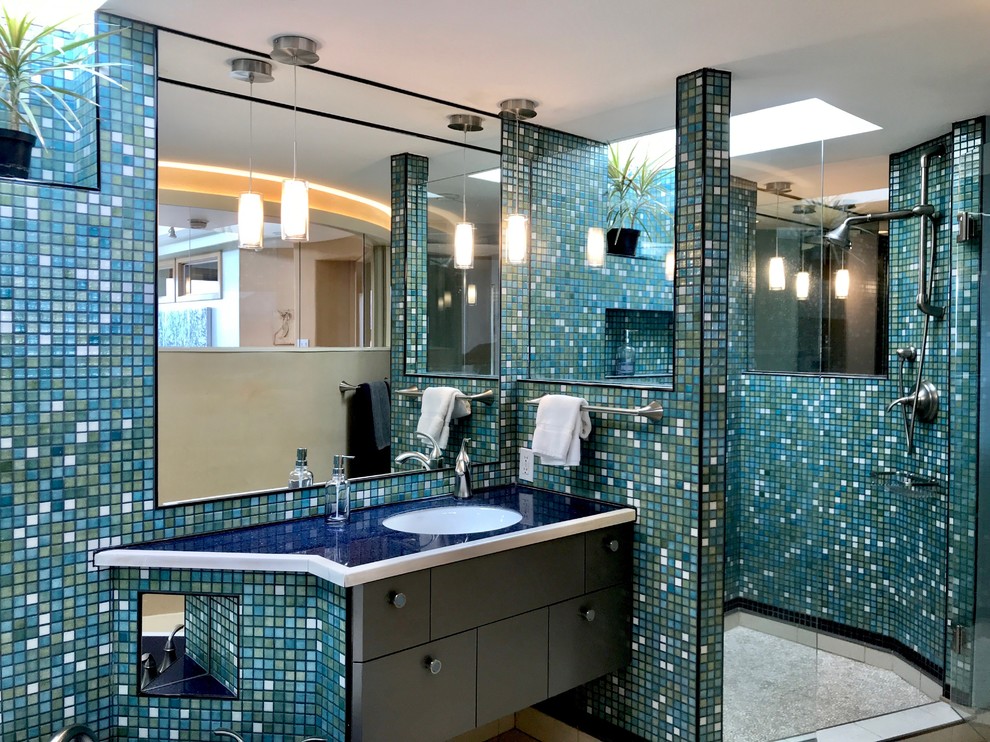 Cette photo montre une salle de bain principale tendance de taille moyenne avec un placard à porte plane, des portes de placard grises, un plan de toilette en verre, un plan de toilette bleu, une douche ouverte, un mur multicolore et un lavabo encastré.