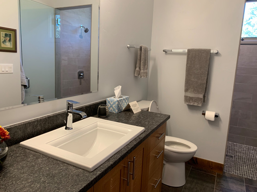 Photo of a medium sized rural ensuite bathroom in Albuquerque with brown cabinets, an alcove shower, a one-piece toilet, grey tiles, porcelain tiles, white walls, porcelain flooring, a built-in sink, granite worktops, black floors, a shower curtain and black worktops.