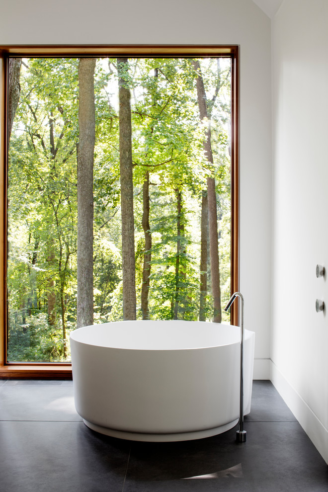 На фото: ванная комната в стиле модернизм с отдельно стоящей ванной, белыми стенами, черным полом и белой столешницей