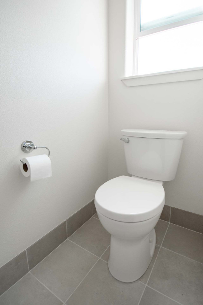 Inspiration pour un grand WC et toilettes craftsman en bois clair avec un placard avec porte à panneau encastré, WC séparés, un carrelage gris, des carreaux de céramique, un mur blanc, un sol en carrelage de céramique, un lavabo encastré, un plan de toilette en quartz modifié, un sol gris, un plan de toilette beige et meuble-lavabo encastré.
