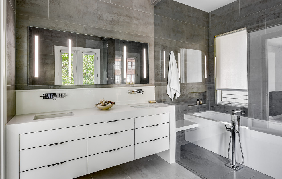 Modelo de cuarto de baño actual de tamaño medio con armarios con paneles lisos, puertas de armario blancas, bañera empotrada, paredes grises y lavabo bajoencimera