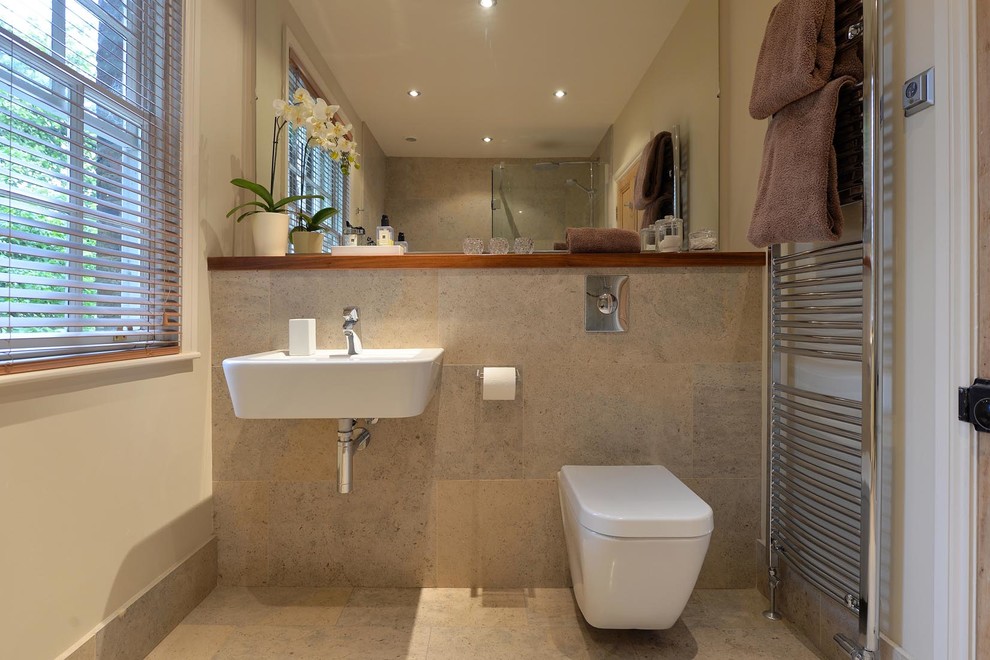 Foto på ett litet funkis en-suite badrum, med ett väggmonterat handfat, träbänkskiva, en dubbeldusch, en vägghängd toalettstol, beige kakel, stenkakel, vita väggar och kalkstensgolv