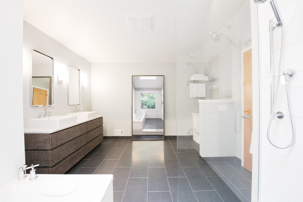 Cette image montre une grande salle de bain principale minimaliste en bois vieilli avec un placard en trompe-l'oeil, WC séparés, un mur gris, un sol en carrelage de céramique, une baignoire en alcôve, un espace douche bain, un carrelage blanc, un carrelage métro, une vasque, un plan de toilette en surface solide, un sol gris et aucune cabine.