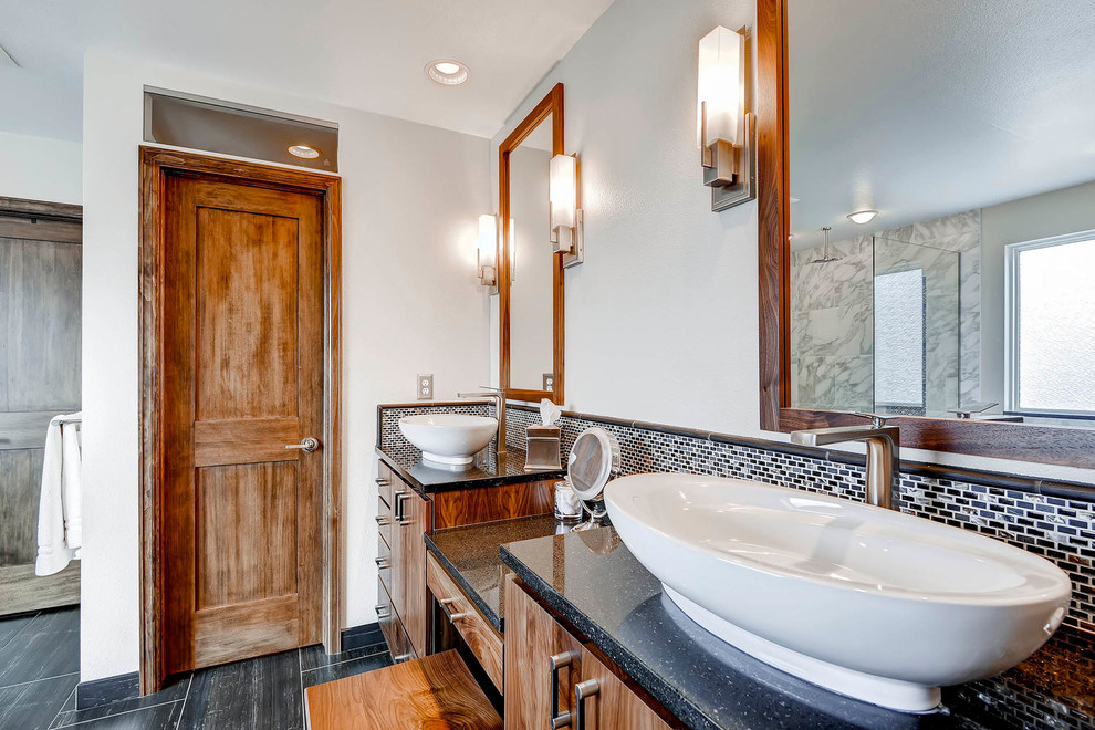 Inspiration for an expansive traditional ensuite bathroom in Denver with a vessel sink, flat-panel cabinets, medium wood cabinets, engineered stone worktops, a built-in bath, a corner shower, a two-piece toilet, black tiles, stone tiles, white walls and porcelain flooring.