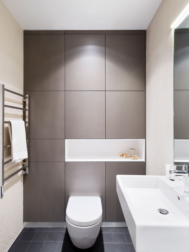 Modelo de cuarto de baño contemporáneo de tamaño medio con sanitario de pared, paredes beige, suelo de baldosas de porcelana, aseo y ducha, lavabo integrado, suelo negro y encimeras blancas