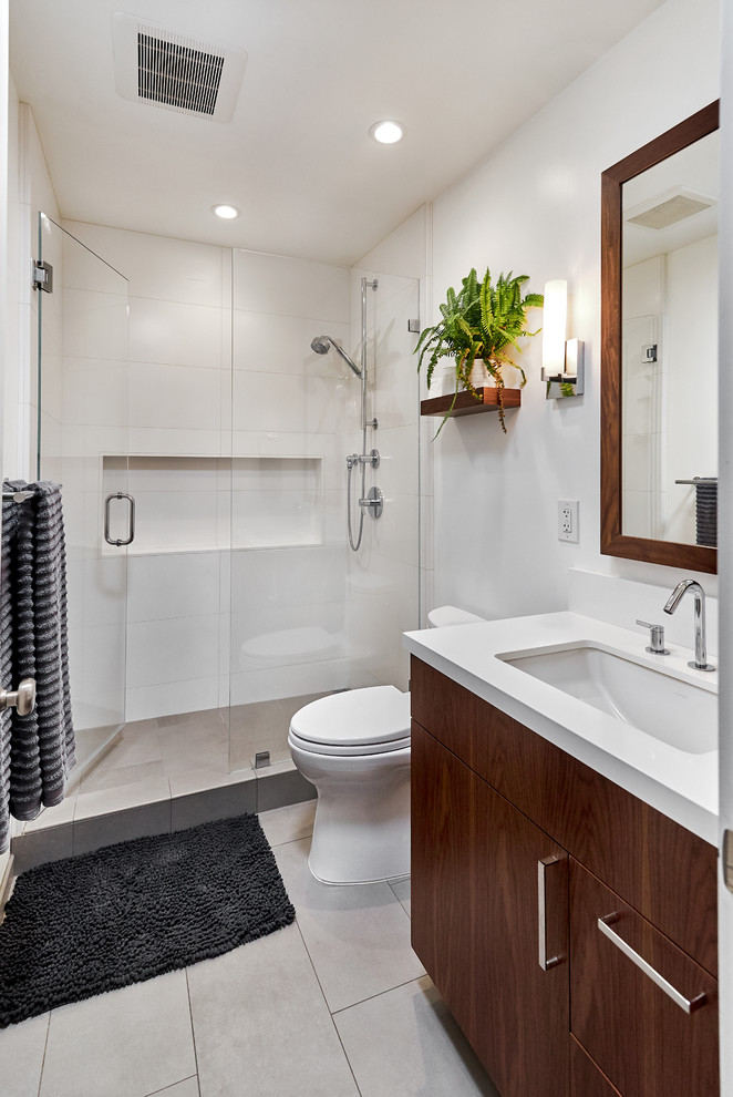 Modernes Duschbad mit flächenbündigen Schrankfronten, dunklen Holzschränken, Duschnische, weißen Fliesen, weißer Wandfarbe, Unterbauwaschbecken, grauem Boden, Falttür-Duschabtrennung und weißer Waschtischplatte in San Francisco