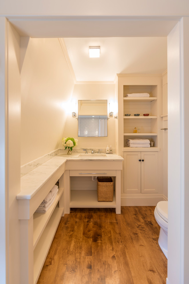 Kleines Klassisches Badezimmer mit weißen Schränken, weißen Fliesen, weißer Wandfarbe und braunem Holzboden in Minneapolis