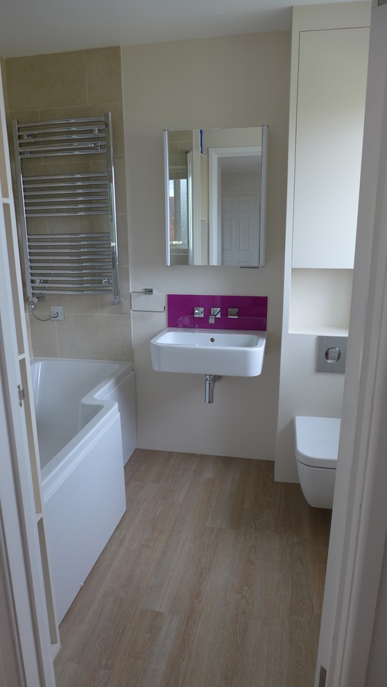 Cette image montre une petite salle de bain design pour enfant avec un lavabo suspendu, un placard à porte plane, des portes de placard grises, une baignoire posée, un combiné douche/baignoire, WC suspendus, un carrelage rose, un mur beige et un sol en linoléum.