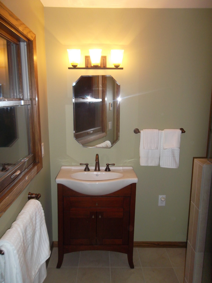 Kleines Klassisches Duschbad mit integriertem Waschbecken, Schrankfronten mit vertiefter Füllung, dunklen Holzschränken, grüner Wandfarbe und Kalkstein in Milwaukee