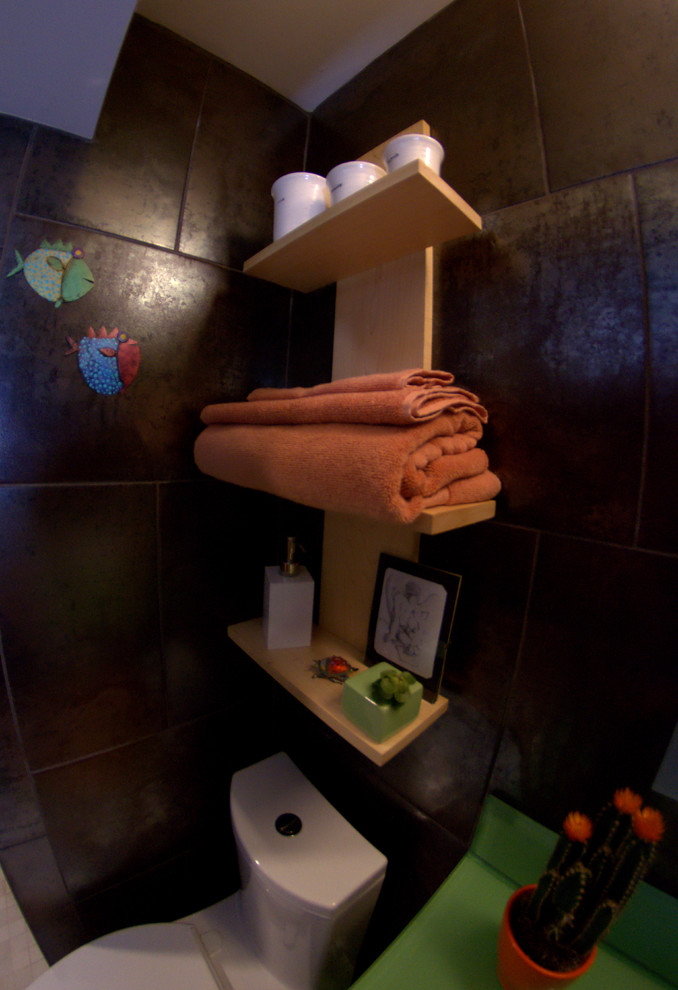 Eklektisk inredning av ett litet badrum, med luckor med glaspanel, gröna skåp, en kantlös dusch, en toalettstol med hel cisternkåpa, brun kakel, cementkakel, klinkergolv i keramik och bänkskiva i glas