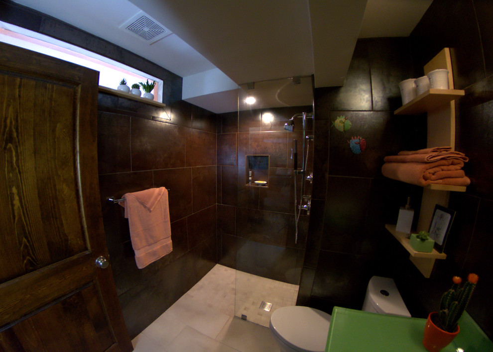 Exempel på ett litet eklektiskt badrum, med luckor med glaspanel, gröna skåp, en kantlös dusch, en toalettstol med hel cisternkåpa, brun kakel, cementkakel, klinkergolv i keramik, bänkskiva i glas, bruna väggar, ett fristående handfat, beiget golv och med dusch som är öppen