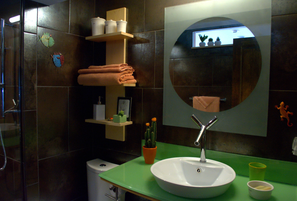 Cette image montre une petite salle de bain bohème avec un placard à porte vitrée, des portes de placards vertess, une douche à l'italienne, WC à poser, un carrelage marron, des carreaux de béton, un sol en carrelage de céramique, un plan de toilette en verre, un mur marron, une vasque, un sol beige et aucune cabine.