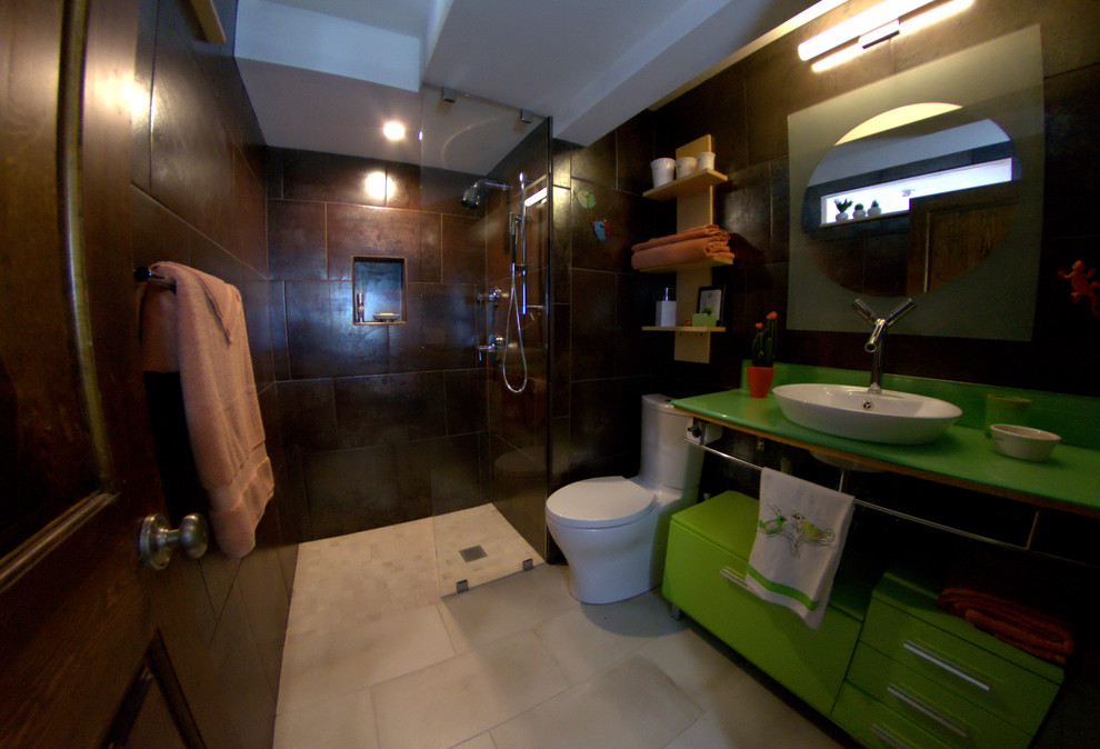 Foto på ett litet funkis en-suite badrum, med luckor med glaspanel, gröna skåp, en kantlös dusch, en toalettstol med hel cisternkåpa, brun kakel, cementkakel, klinkergolv i keramik, bänkskiva i glas, bruna väggar, beiget golv, ett fristående handfat och med dusch som är öppen