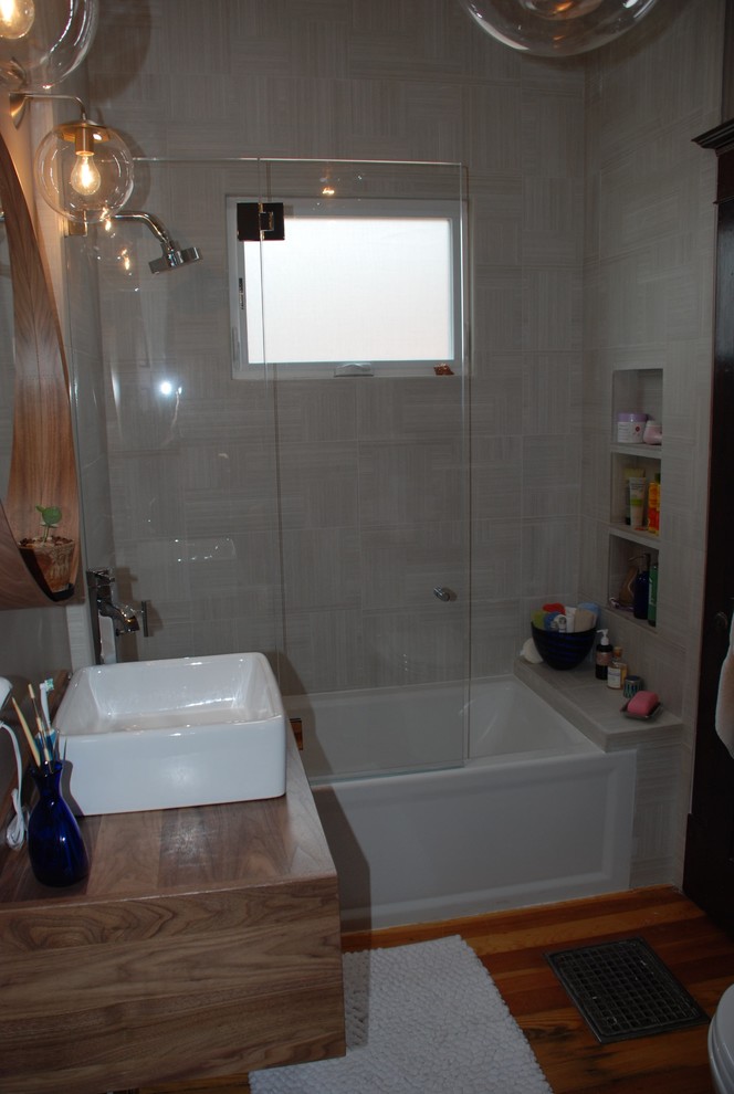 Photo of a small contemporary family bathroom in Denver with flat-panel cabinets, an alcove bath, a shower/bath combination, a vessel sink, wooden worktops, a one-piece toilet, grey walls, medium hardwood flooring, medium wood cabinets, white tiles, porcelain tiles and a hinged door.