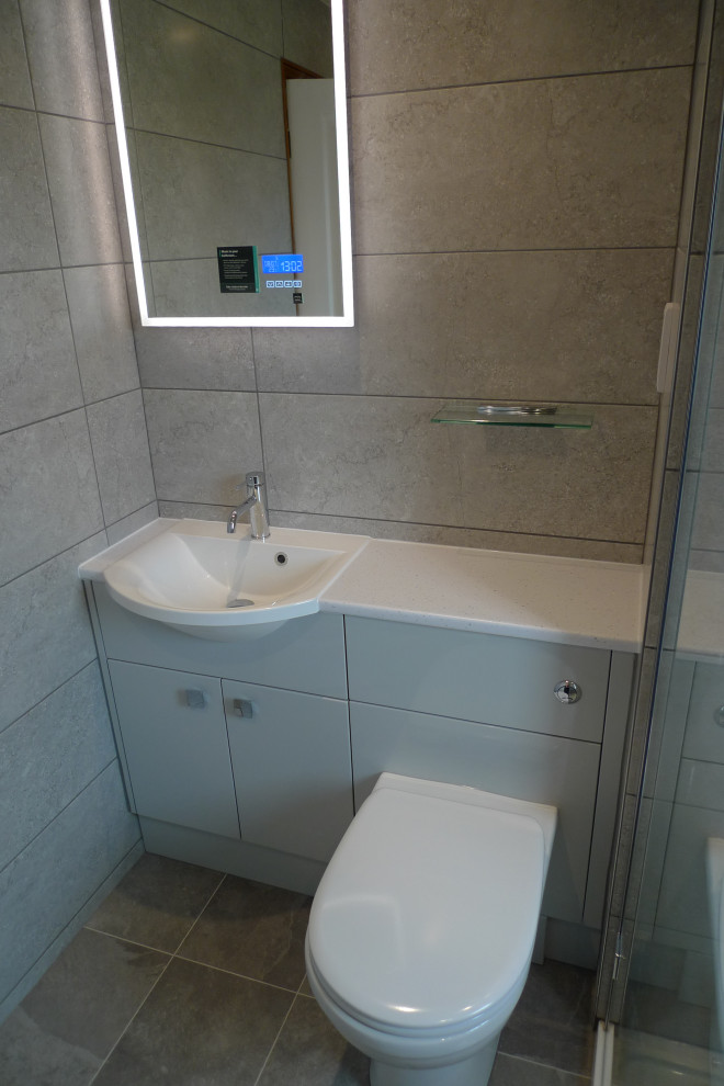 Bild på ett litet funkis vit vitt badrum med dusch, med släta luckor, grå skåp, en öppen dusch, en toalettstol med hel cisternkåpa, keramikplattor, vinylgolv, ett nedsänkt handfat, bänkskiva i akrylsten och grått golv