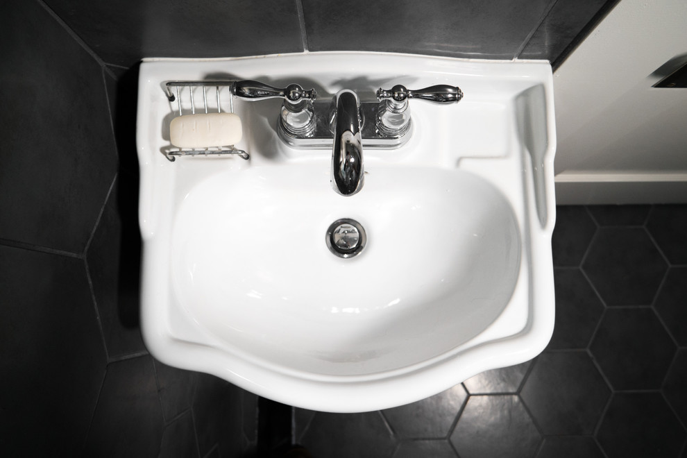 Foto på ett litet industriellt badrum, med en toalettstol med separat cisternkåpa, svart och vit kakel, porslinskakel, vita väggar, klinkergolv i porslin och ett piedestal handfat