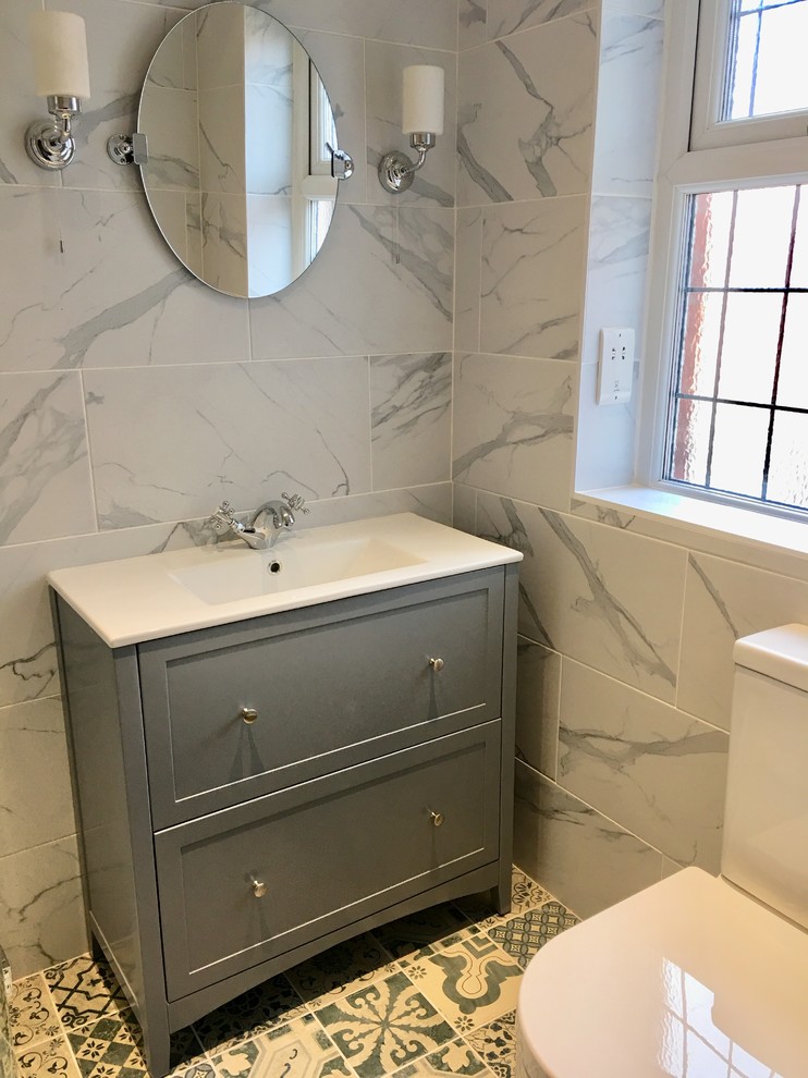 Design ideas for a small contemporary ensuite bathroom in Other with freestanding cabinets, grey cabinets, a corner shower, a two-piece toilet, grey tiles, porcelain tiles, grey walls, porcelain flooring, a built-in sink, solid surface worktops, blue floors, a hinged door and white worktops.