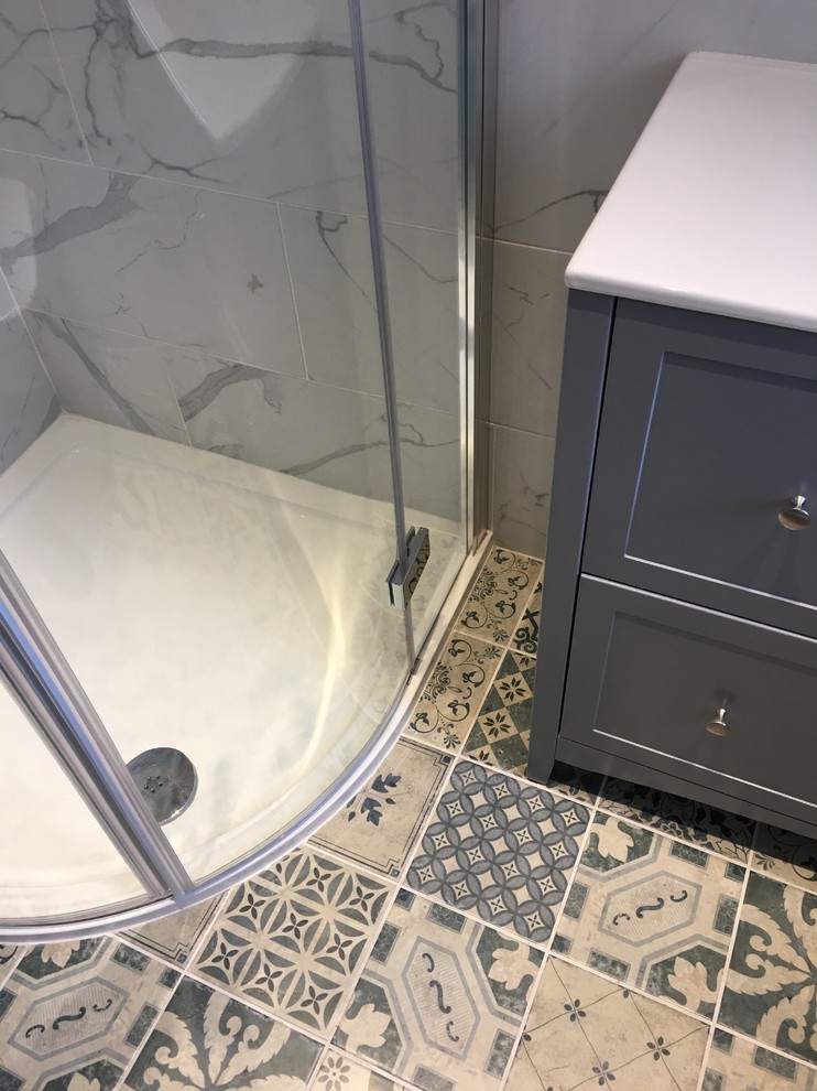 This is an example of a small contemporary ensuite bathroom in Other with freestanding cabinets, grey cabinets, a corner shower, a two-piece toilet, grey tiles, porcelain tiles, grey walls, porcelain flooring, a built-in sink, solid surface worktops, blue floors, a hinged door and white worktops.