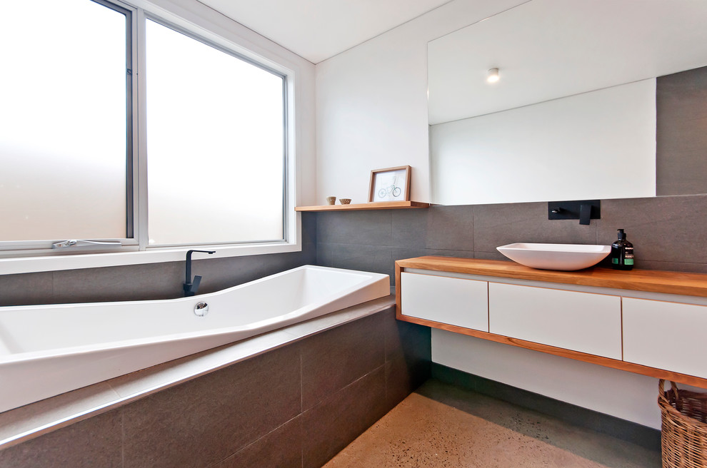 Design ideas for a medium sized contemporary ensuite bathroom in Geelong with wooden worktops, grey tiles, ceramic tiles, a built-in bath, a walk-in shower, a one-piece toilet, a vessel sink, white walls and concrete flooring.
