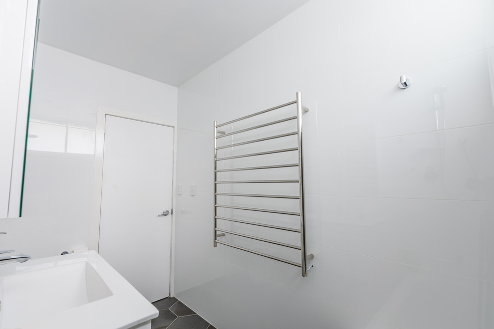 Пример оригинального дизайна: маленькая ванная комната в стиле модернизм с плоскими фасадами, ванной в нише, душем над ванной, серой плиткой, керамогранитной плиткой, белыми стенами, полом из керамогранита и монолитной раковиной для на участке и в саду