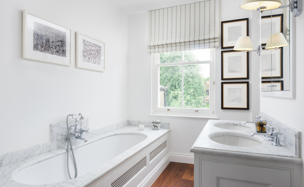 Photo of a classic bathroom in London with white cabinets, a submerged bath, white walls, dark hardwood flooring, a submerged sink, brown floors and white worktops.