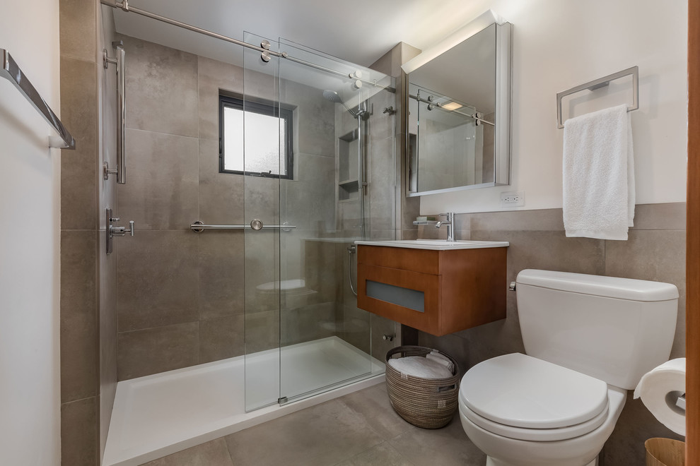 Photo of a small modern bathroom in Other with shaker cabinets, medium wood cabinets, an alcove shower, a one-piece toilet, beige tiles, porcelain tiles, white walls, porcelain flooring, a wall-mounted sink, beige floors and a sliding door.