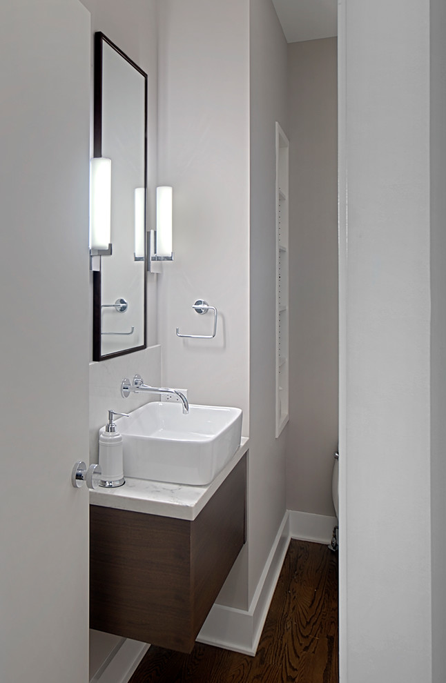 Cette image montre un petit WC et toilettes design en bois foncé avec un placard à porte plane, un mur gris, parquet foncé, une vasque, un plan de toilette en quartz modifié, un sol marron, un plan de toilette blanc et meuble-lavabo suspendu.