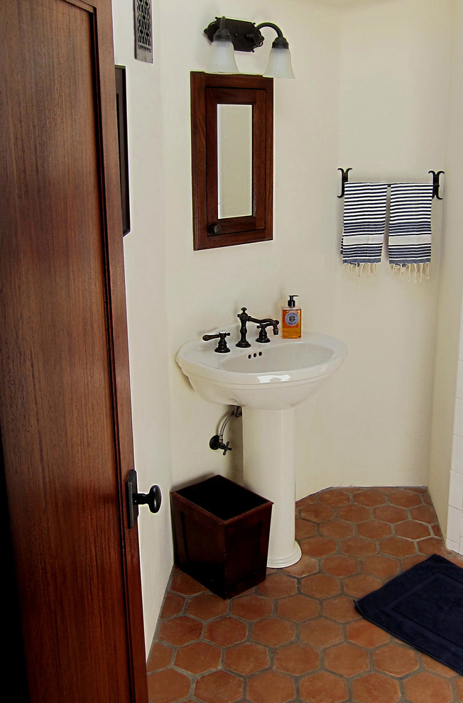 サンタバーバラにあるお手頃価格の小さな地中海スタイルのおしゃれなマスターバスルーム (コーナー設置型シャワー、分離型トイレ、テラコッタタイル、白い壁、テラコッタタイルの床、ペデスタルシンク、オープンシェルフ、中間色木目調キャビネット、白いタイル、赤い床、白い洗面カウンター) の写真