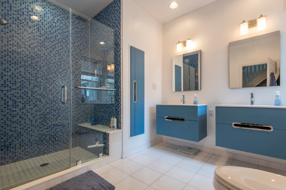 Свежая идея для дизайна: большая ванная комната в современном стиле с плоскими фасадами, синими фасадами, душем в нише, синей плиткой, белыми стенами, полом из керамогранита, белым полом, душем с распашными дверями, белой столешницей, сиденьем для душа, тумбой под две раковины, подвесной тумбой и душевой кабиной - отличное фото интерьера