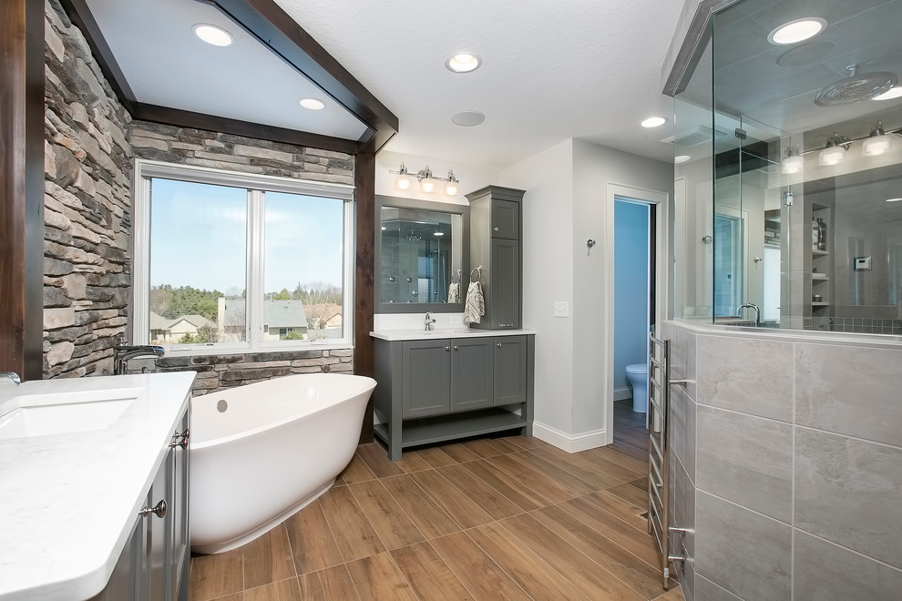 Example of a large transitional master gray tile and porcelain tile medium tone wood floor and brown floor bathroom design in Minneapolis with shaker cabinets, gray cabinets, gray walls, an undermount sink, quartz countertops, a hinged shower door and white countertops