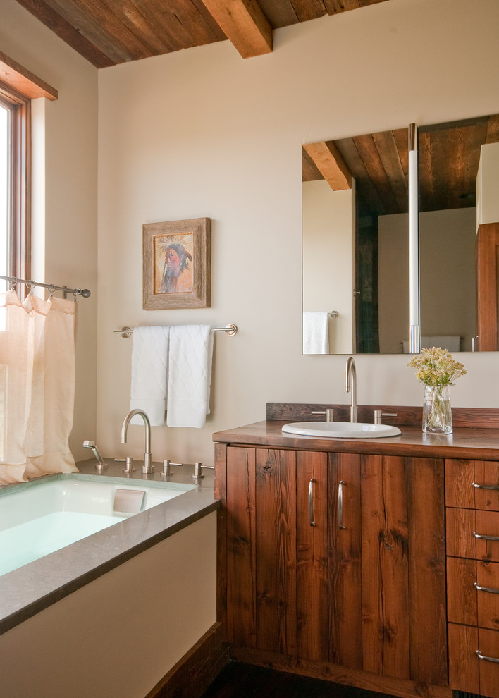 Diseño de cuarto de baño rural con lavabo encastrado, armarios con paneles lisos, puertas de armario de madera oscura, encimera de madera, bañera encastrada sin remate y paredes beige