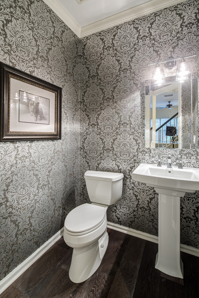 Inredning av ett klassiskt litet toalett, med en toalettstol med separat cisternkåpa, grå väggar, mellanmörkt trägolv, ett piedestal handfat och brunt golv