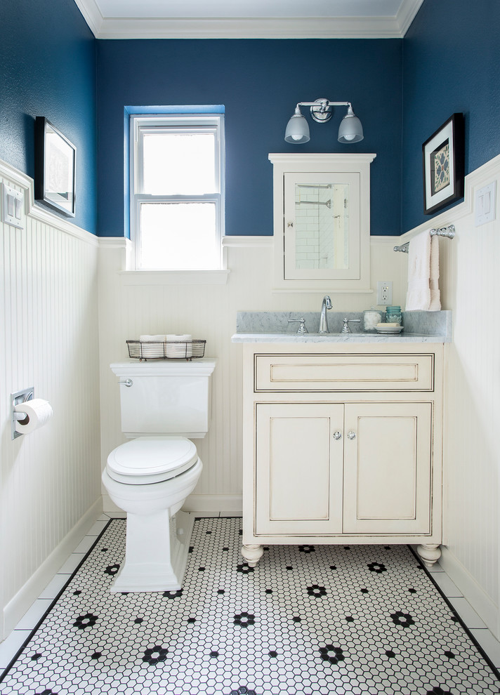 Inredning av ett klassiskt litet badrum med dusch, med luckor med profilerade fronter, vita skåp, blå väggar, mosaikgolv och ett undermonterad handfat
