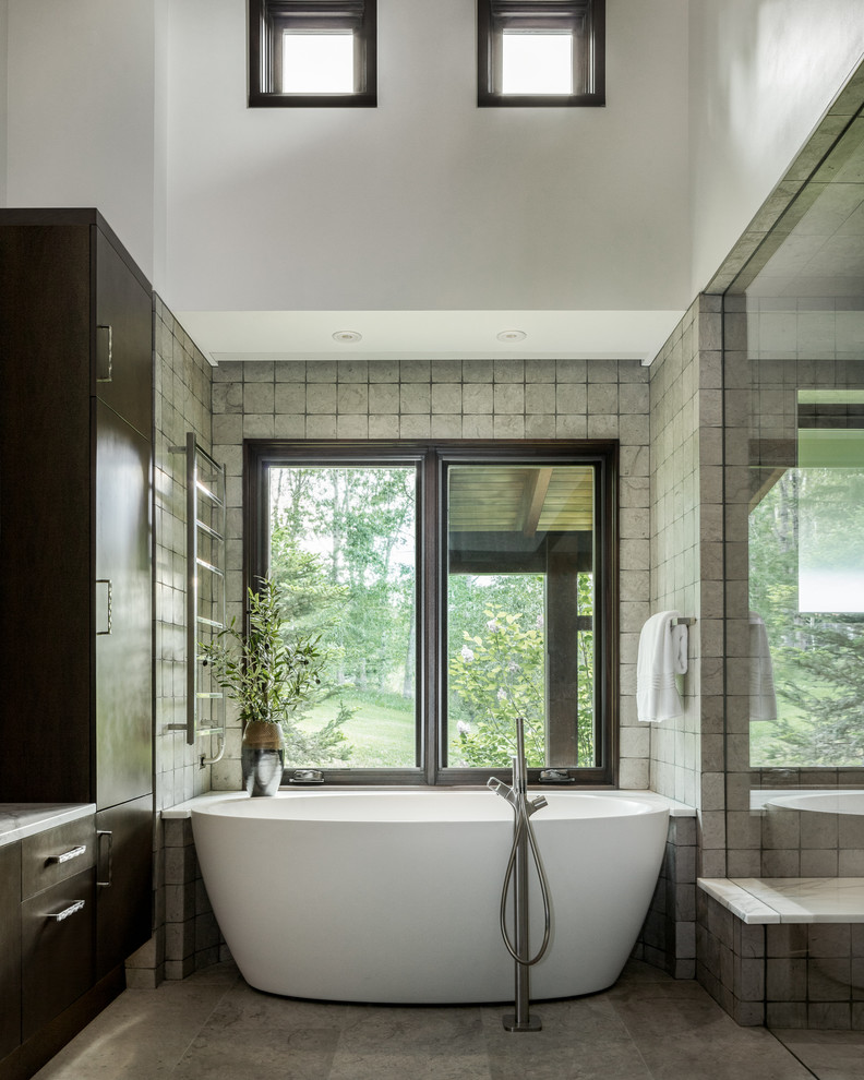 Modernes Badezimmer mit flächenbündigen Schrankfronten, dunklen Holzschränken, freistehender Badewanne, grauen Fliesen, weißer Wandfarbe, grauem Boden und weißer Waschtischplatte in Denver