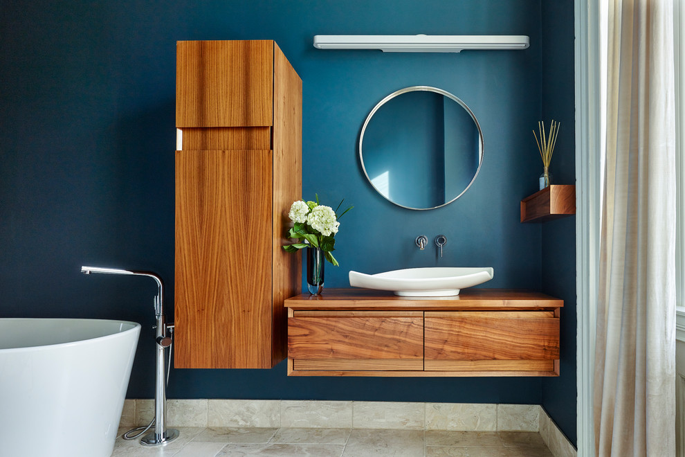 Modern inredning av ett en-suite badrum, med ett fristående handfat, skåp i mellenmörkt trä, ett fristående badkar och blå väggar