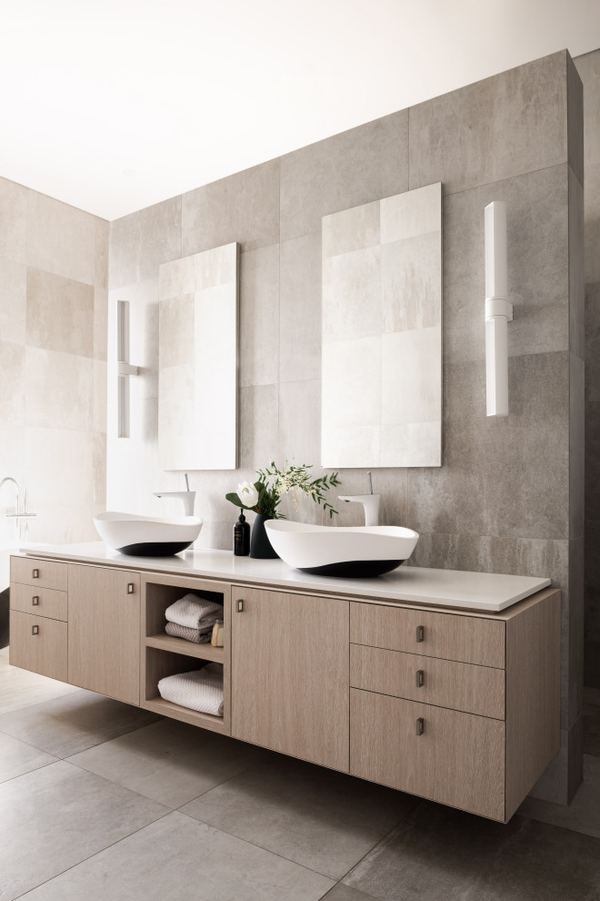 Foto de cuarto de baño principal contemporáneo con armarios con paneles lisos, puertas de armario de madera clara, baldosas y/o azulejos grises, paredes grises, lavabo sobreencimera, suelo gris y encimeras blancas