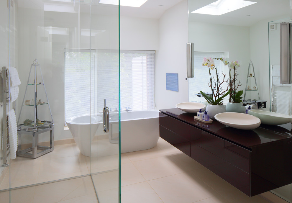 Idéer för att renovera ett stort funkis en-suite badrum, med släta luckor, ett fristående badkar, en öppen dusch, en vägghängd toalettstol, beige kakel, porslinskakel, vita väggar, klinkergolv i porslin, ett konsol handfat och bänkskiva i glas