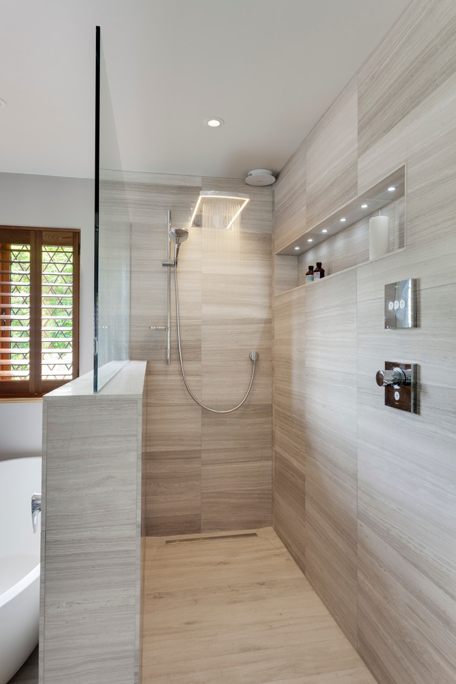 Modern inredning av ett stort en-suite badrum, med släta luckor, skåp i ljust trä, ett fristående badkar, en öppen dusch, grå kakel, stenhäll, grå väggar, kalkstensgolv och marmorbänkskiva