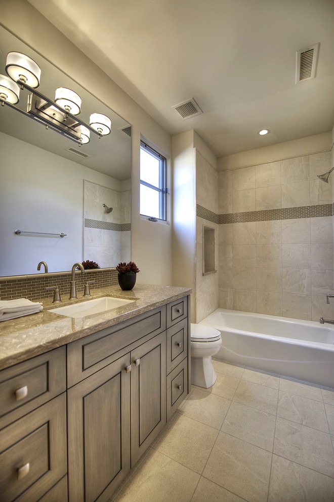 Immagine di una stanza da bagno chic di medie dimensioni con lavabo sottopiano, ante grigie, vasca/doccia e WC monopezzo