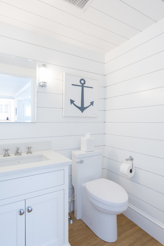 Small coastal shower room bathroom in Boston with shaker cabinets, white cabinets, a one-piece toilet, white tiles, white walls, medium hardwood flooring, a submerged sink, engineered stone worktops, white worktops and brown floors.
