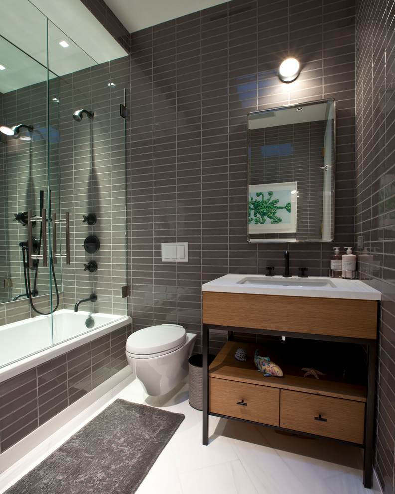 Medium sized contemporary shower room bathroom in New York with flat-panel cabinets, medium wood cabinets, an alcove bath, an alcove shower, a wall mounted toilet, grey tiles, ceramic tiles, grey walls, marble flooring, a submerged sink and solid surface worktops.