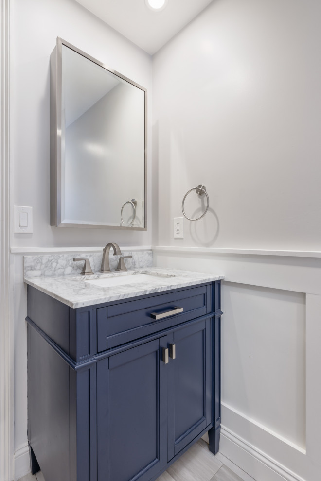 На фото: ванная комната среднего размера в стиле неоклассика (современная классика) с фасадами в стиле шейкер, синими фасадами, душем в нише, раздельным унитазом, белой плиткой, плиткой кабанчик, серыми стенами, полом из керамогранита, душевой кабиной, врезной раковиной, мраморной столешницей, разноцветным полом, душем с распашными дверями, разноцветной столешницей, тумбой под одну раковину, напольной тумбой и панелями на стенах