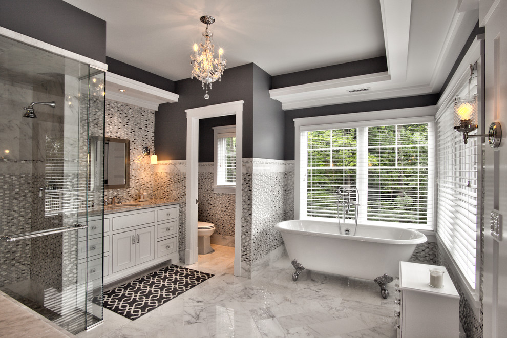 Foto på ett mycket stort funkis en-suite badrum, med ett undermonterad handfat, möbel-liknande, vita skåp, marmorbänkskiva, ett fristående badkar, en kantlös dusch, en toalettstol med separat cisternkåpa, vit kakel, glaskakel, grå väggar och marmorgolv