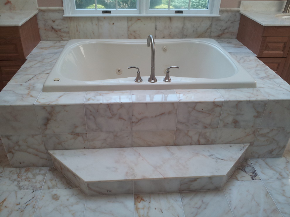 Inspiration for a transitional master beige tile and multicolored tile marble floor drop-in bathtub remodel in New York with raised-panel cabinets, medium tone wood cabinets, an undermount sink and marble countertops