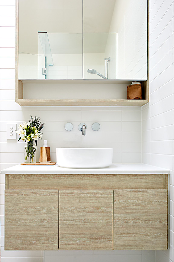 Bild på ett litet maritimt badrum med dusch, med släta luckor, skåp i ljust trä, en hörndusch, en vägghängd toalettstol, keramikplattor, mosaikgolv, ett fristående handfat och bänkskiva i akrylsten