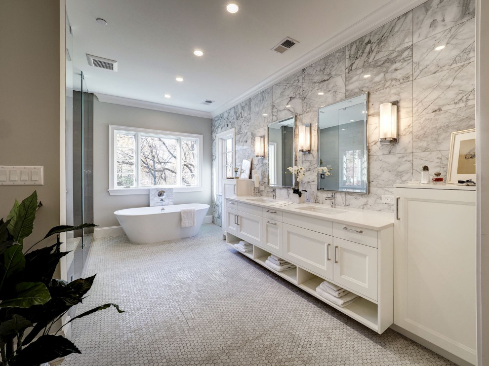 На фото: огромная главная ванная комната в стиле неоклассика (современная классика) с фасадами в стиле шейкер, белыми фасадами, отдельно стоящей ванной, душем в нише, серой плиткой, керамогранитной плиткой, серыми стенами, врезной раковиной, серым полом, душем с распашными дверями и белой столешницей с