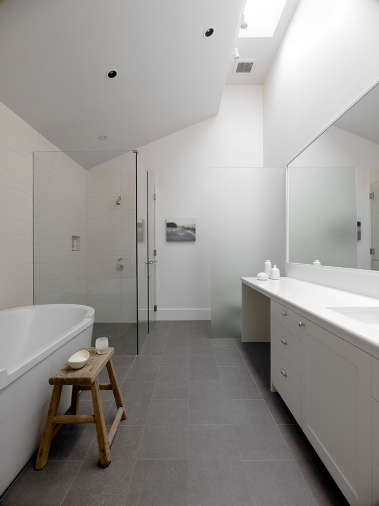 Modelo de cuarto de baño minimalista con ducha a ras de suelo, bañera exenta, suelo gris y encimeras blancas