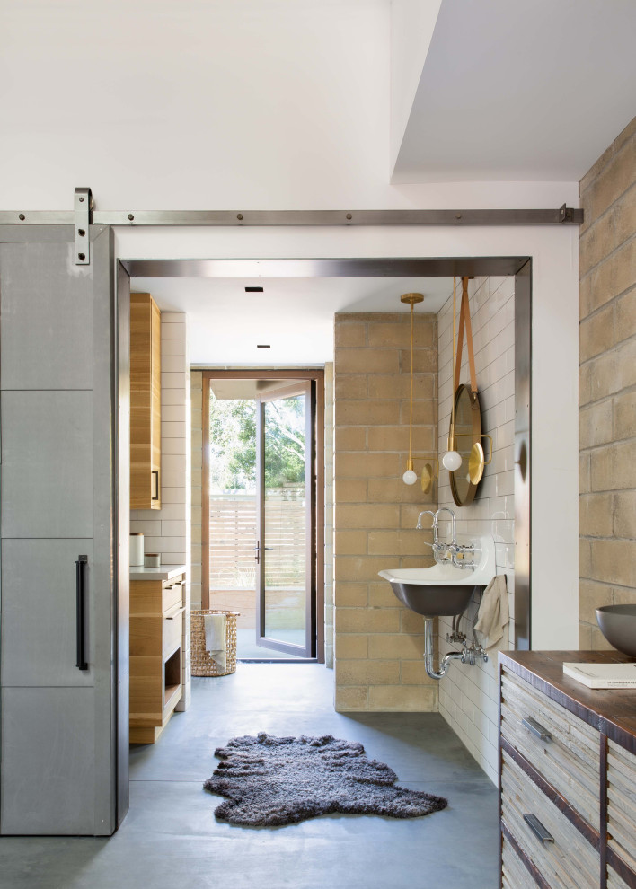 Пример оригинального дизайна: главная ванная комната в стиле кантри с кирпичными стенами, бежевой плиткой, белыми стенами, бетонным полом, подвесной раковиной, серым полом и тумбой под две раковины