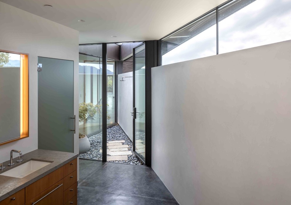 Идея дизайна: большая главная ванная комната в стиле модернизм с плоскими фасадами, фасадами цвета дерева среднего тона, отдельно стоящей ванной, белыми стенами, бетонным полом, врезной раковиной и серым полом