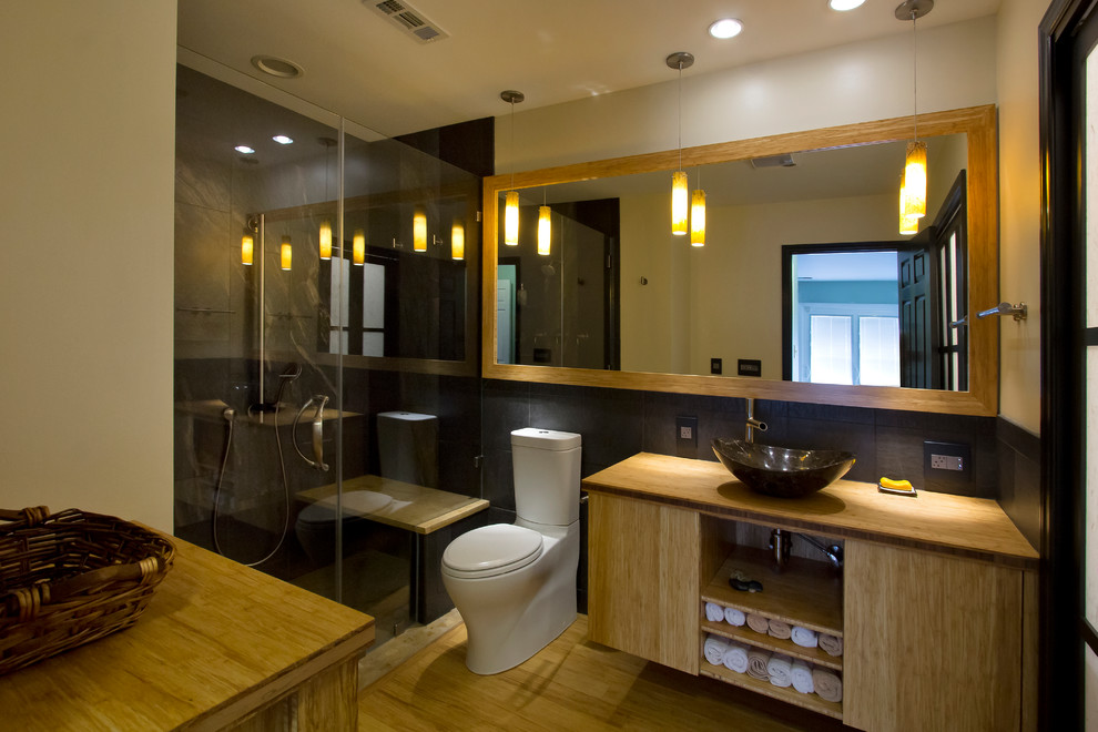 Modern inredning av ett mellanstort gul gult en-suite badrum, med ett fristående handfat, skåp i ljust trä, träbänkskiva, en kantlös dusch, en toalettstol med separat cisternkåpa, porslinskakel, gula väggar, bambugolv, släta luckor, svart kakel, gult golv och dusch med gångjärnsdörr
